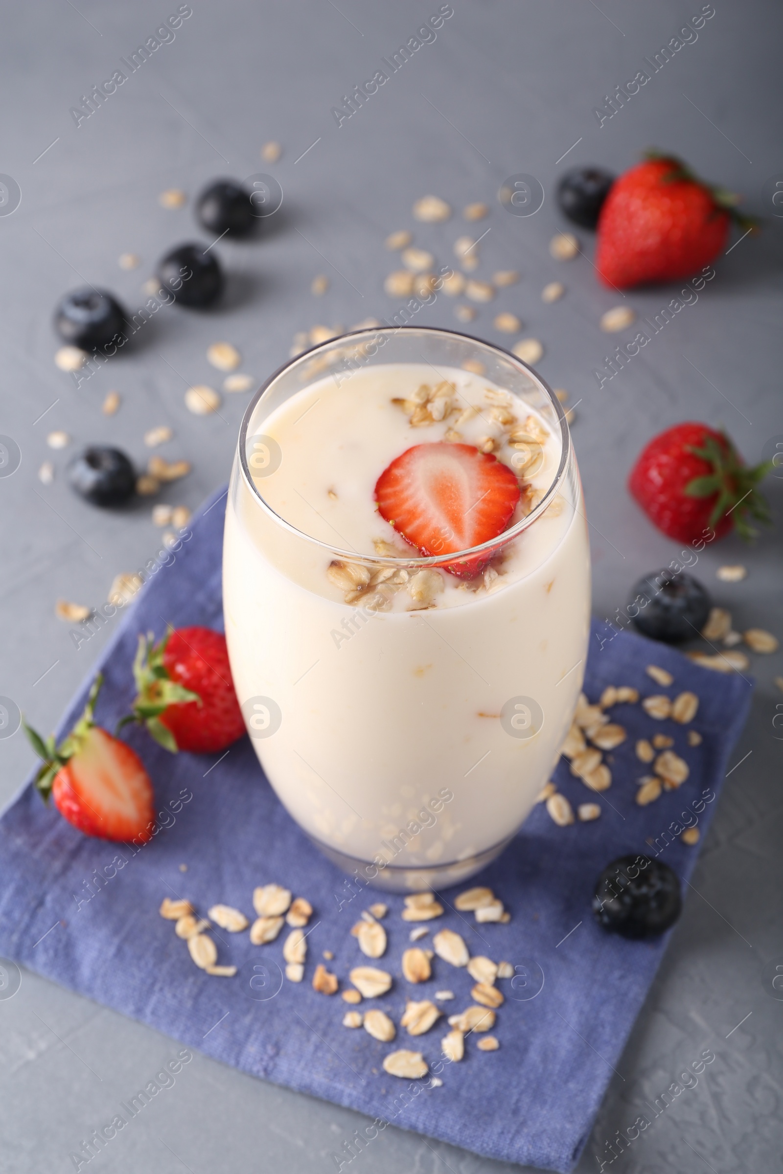 Photo of Tasty yogurt in glass, oats and berries on grey table