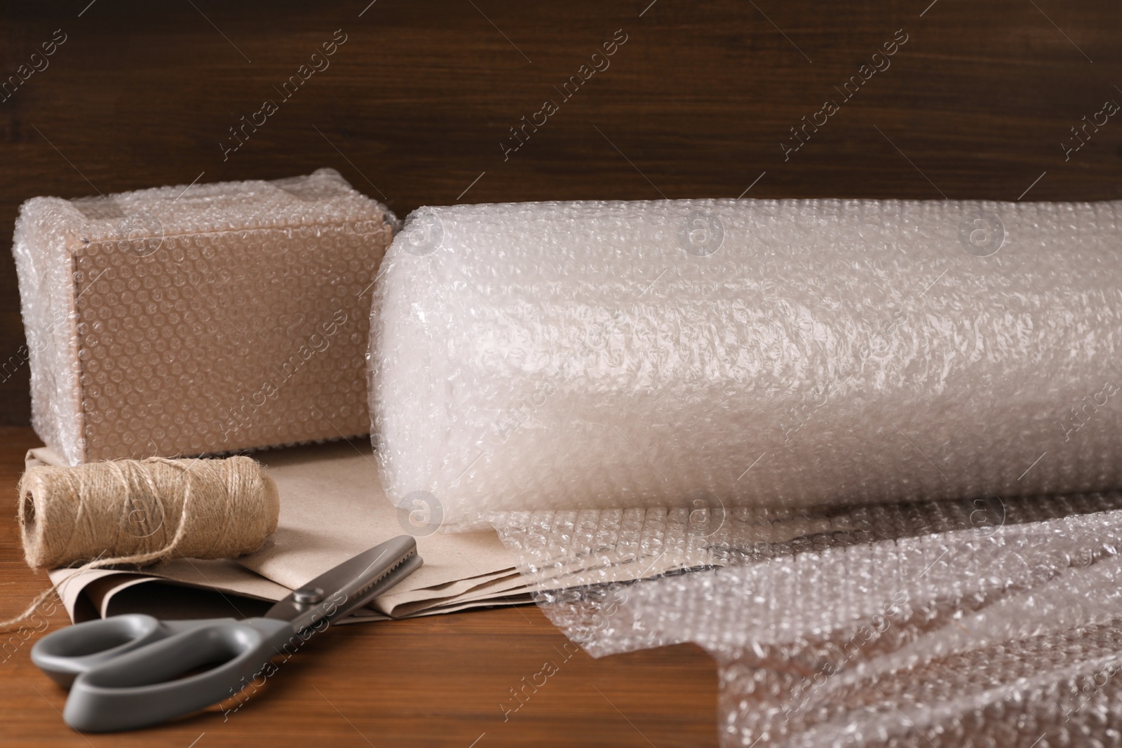 Photo of Scissors, twine, paper, roll of bubble wrap and packed box on wooden table