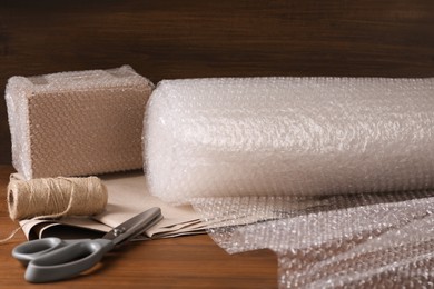 Photo of Scissors, twine, paper, roll of bubble wrap and packed box on wooden table