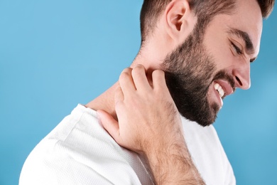 Photo of Young man scratching neck on color background. Allergies symptoms