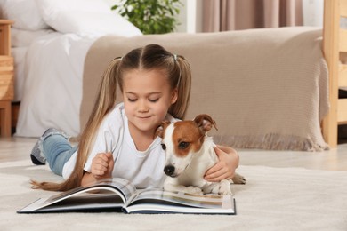 Photo of Cute girl reading book on floor with her dog at home. Adorable pet