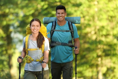 Couple with backpacks and trekking poles hiking in forest