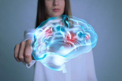 Young woman pointing at digital image of brain on grey background, closeup