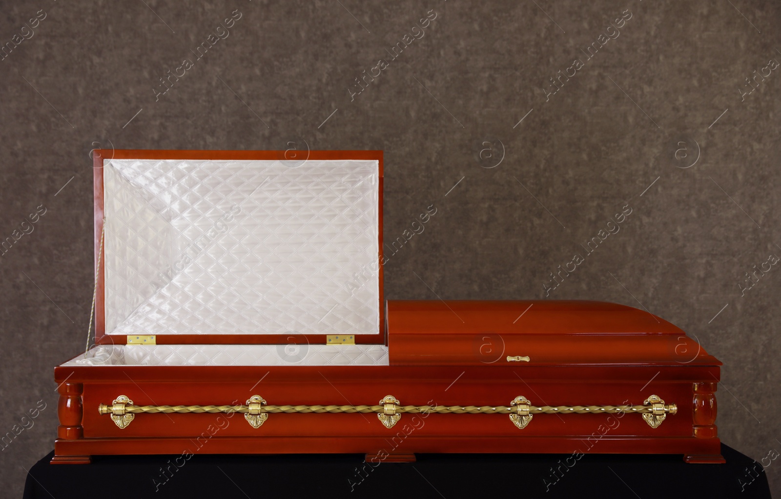 Photo of Open wooden funeral casket on stand at grey wall