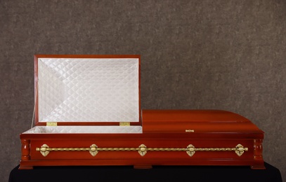 Open wooden funeral casket on stand at grey wall