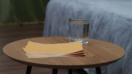 Pepper plasters and glass of water on wooden coffee table indoors