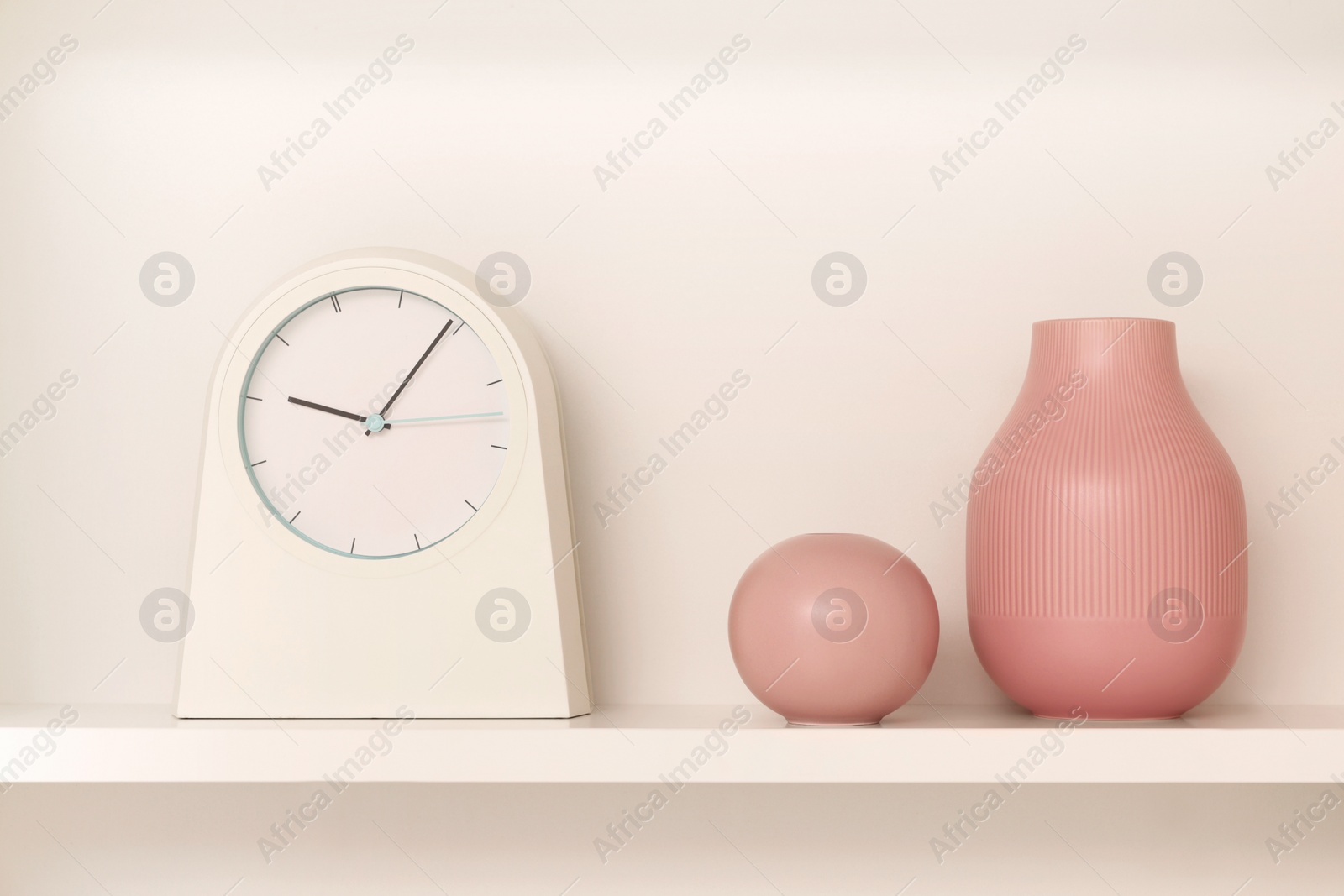 Photo of Shelf with stylish watch and vases near beige wall. Interior design