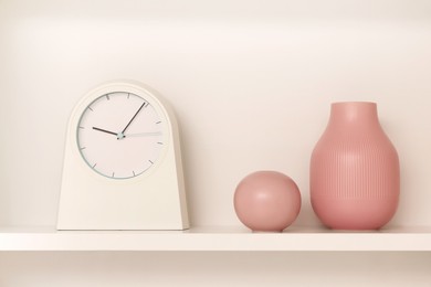 Shelf with stylish watch and vases near beige wall. Interior design