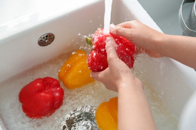 Photo of Woman washing fresh bell peppers in kitchen sink, closeup