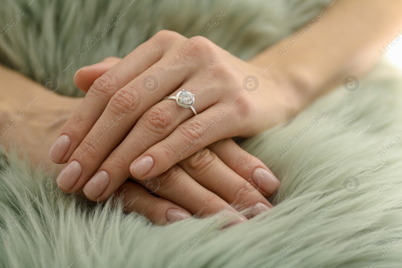 Photo of Young woman wearing beautiful engagement ring on faux fur rug, closeup