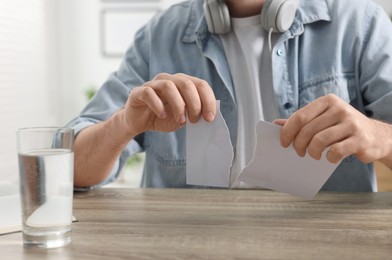 Photo of Man ripping photo at table indoors, closeup. Divorce concept