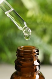 Pipette with oil over bottle on blurred background