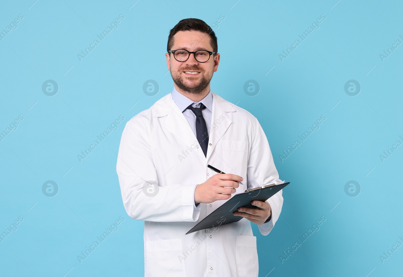 Photo of Smiling doctor with pen and clipboard on light blue background