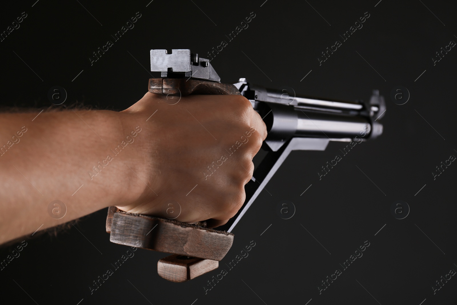 Photo of Gun shooting sport. Man aiming standard pistol on dark background, closeup