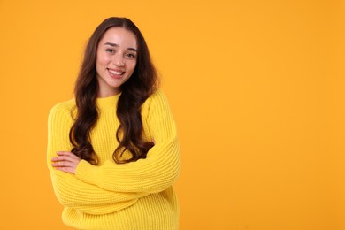 Beautiful young woman in stylish warm sweater on orange background, space for text