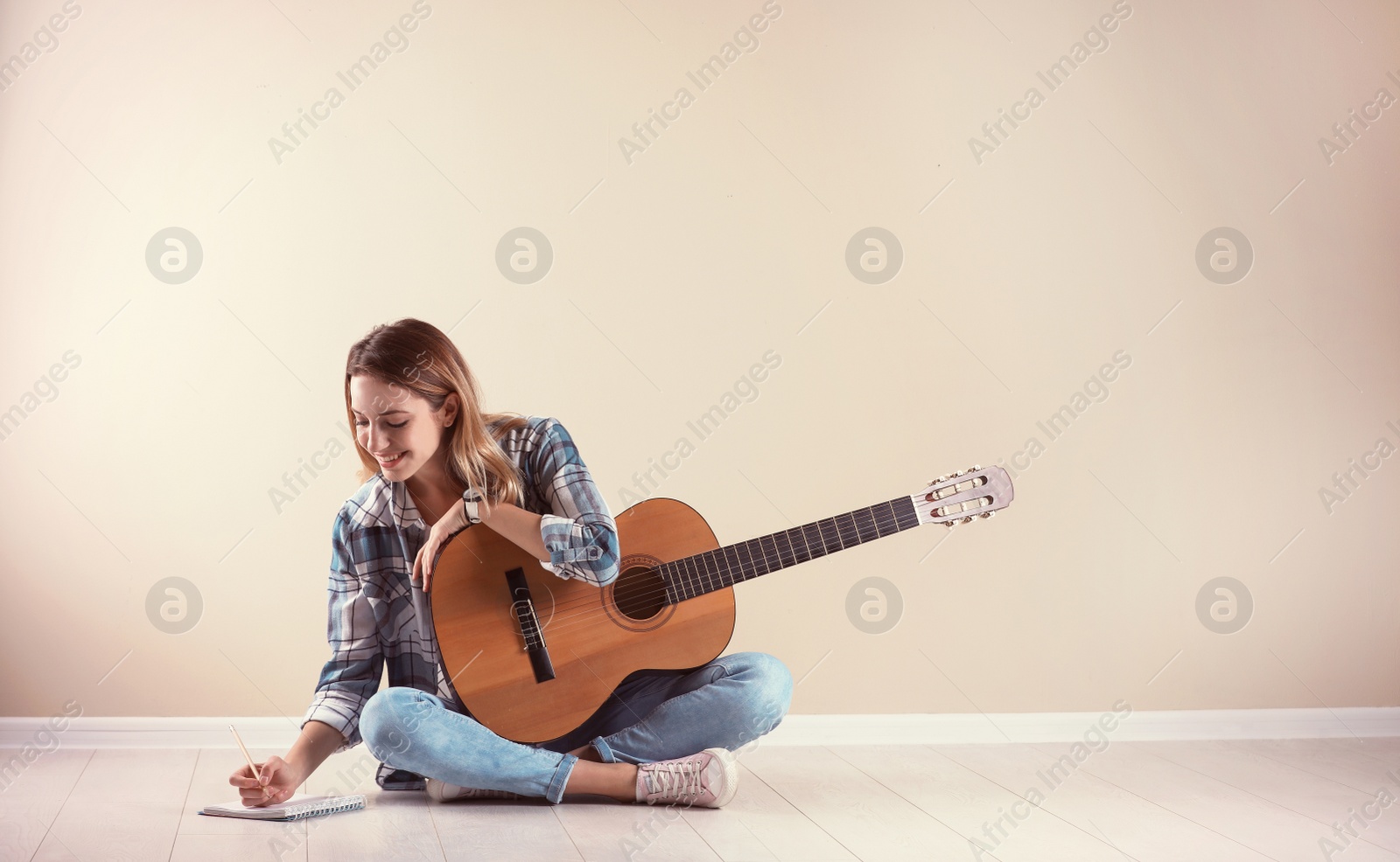 Photo of Young woman with acoustic guitar composing song near grey wall. Space for text