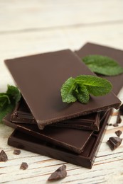 Photo of Tasty dark chocolate pieces with mint on white wooden table, closeup