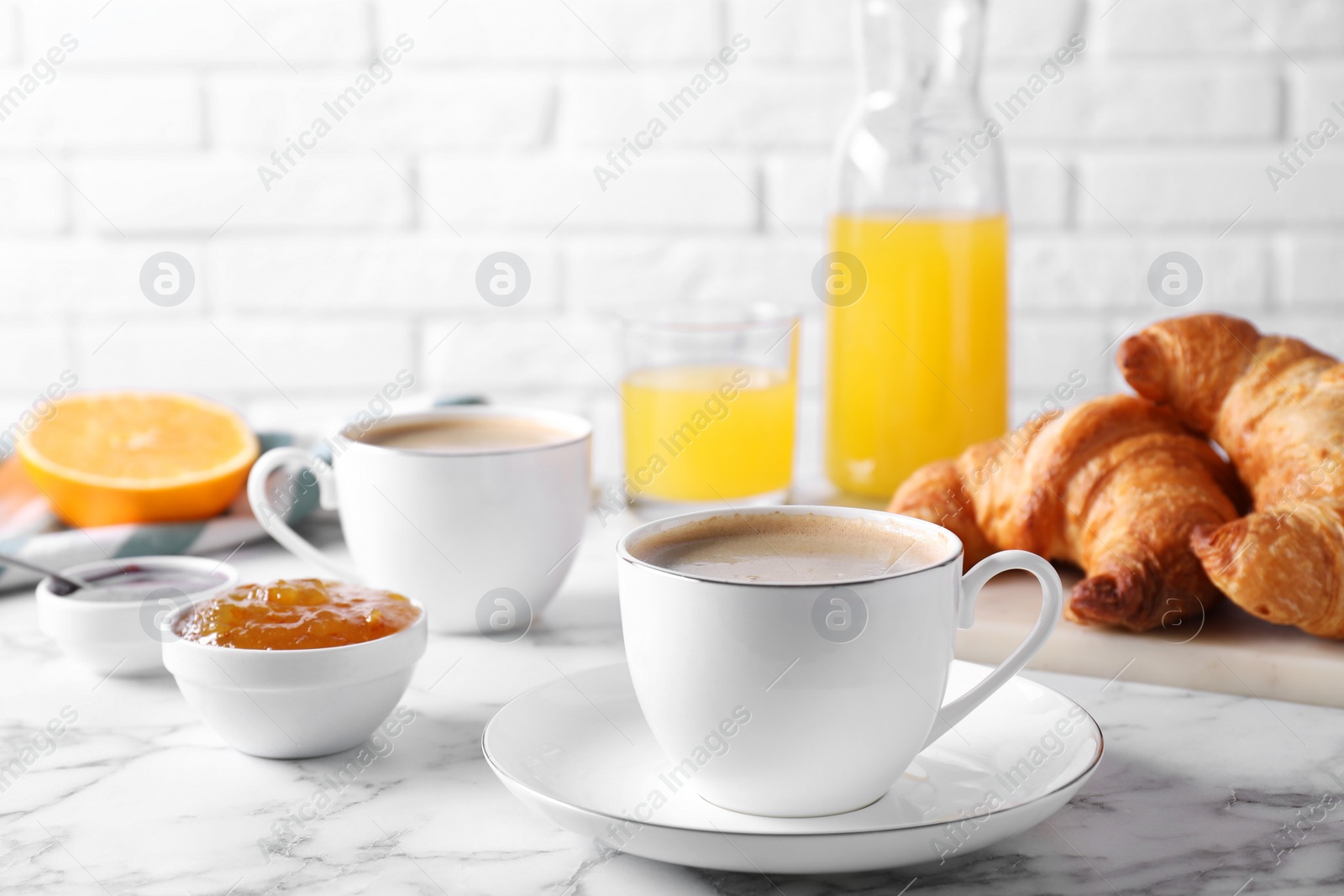 Photo of Tasty breakfast. Cups of coffee, fresh croissants and jam on white marble table