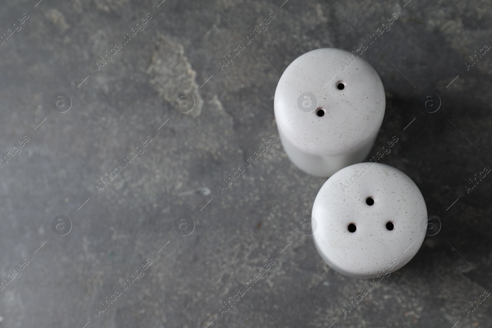 Photo of Salt and pepper shakers on dark textured table, above view. Space for text