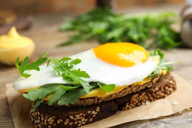 Delicious sandwich with arugula and egg on wooden table, closeup