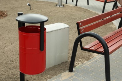 Photo of Red metal trash bin near wooden bench in city park
