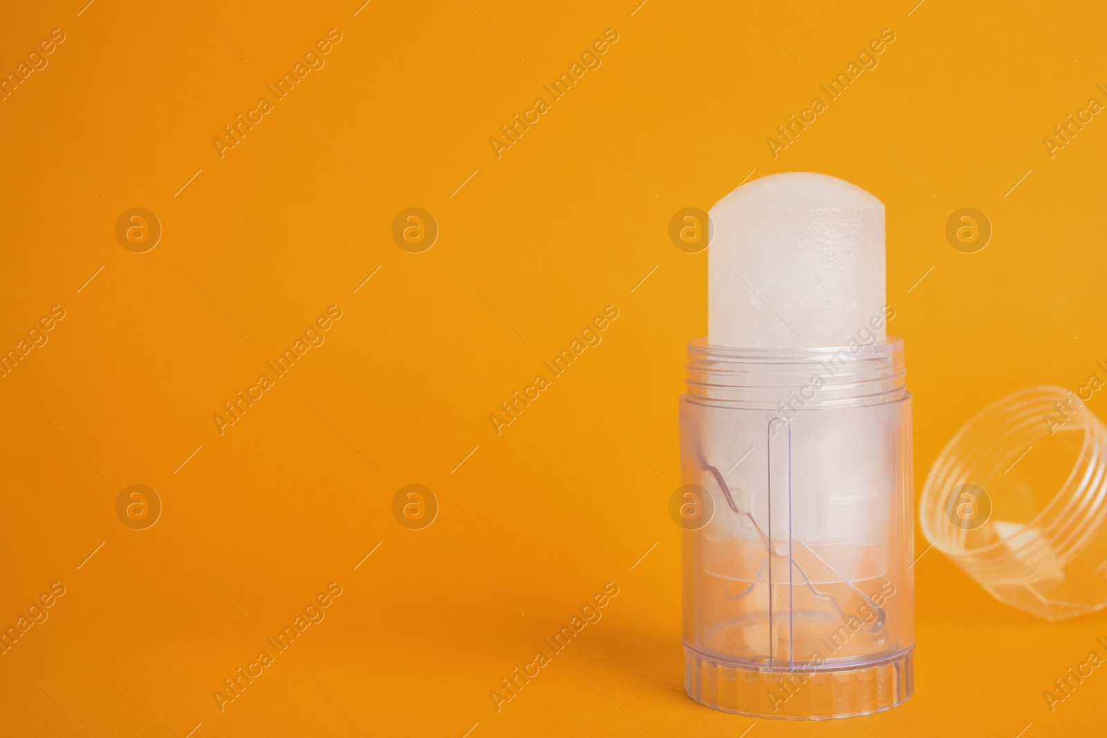 Photo of Natural crystal alum stick deodorant and cap on orange background. Space for text