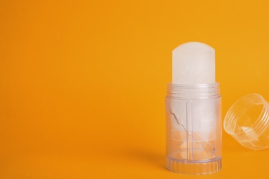 Photo of Natural crystal alum stick deodorant and cap on orange background. Space for text