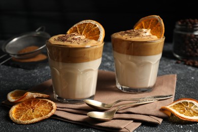 Glasses of delicious dalgona coffee with dry orange and chocolate on grey textured table