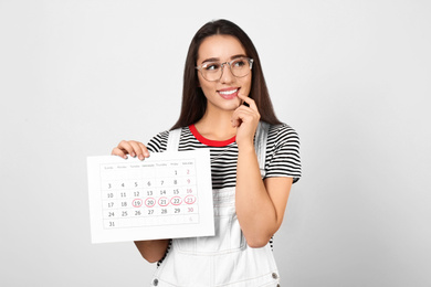 Photo of Young woman holding calendar with marked menstrual cycle days on light background