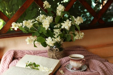 Photo of Bouquet of beautiful jasmine flowers in vase, open book and aromatic tea on fabric indoors
