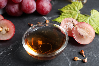 Photo of Bowl of natural grape seed oil on dark table. Organic cosmetic