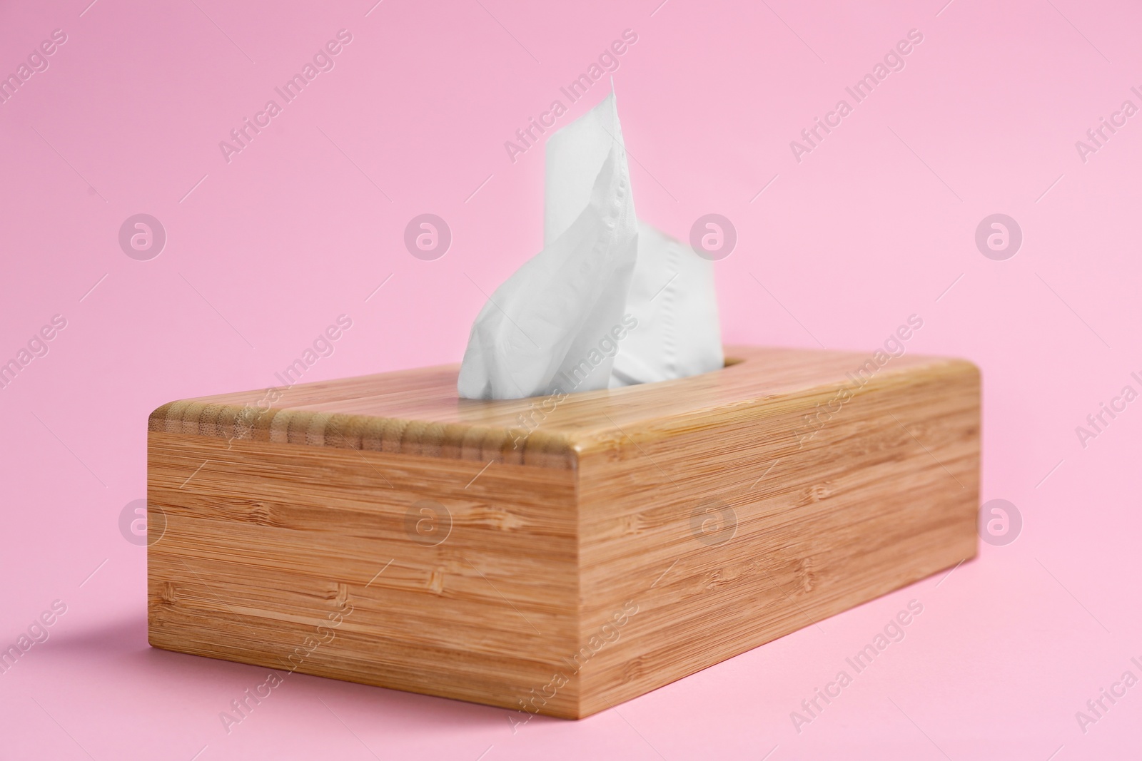 Photo of Wooden holder with paper tissues on pink background