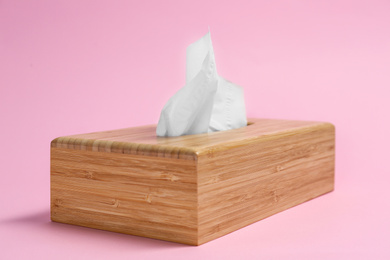 Photo of Wooden holder with paper tissues on pink background