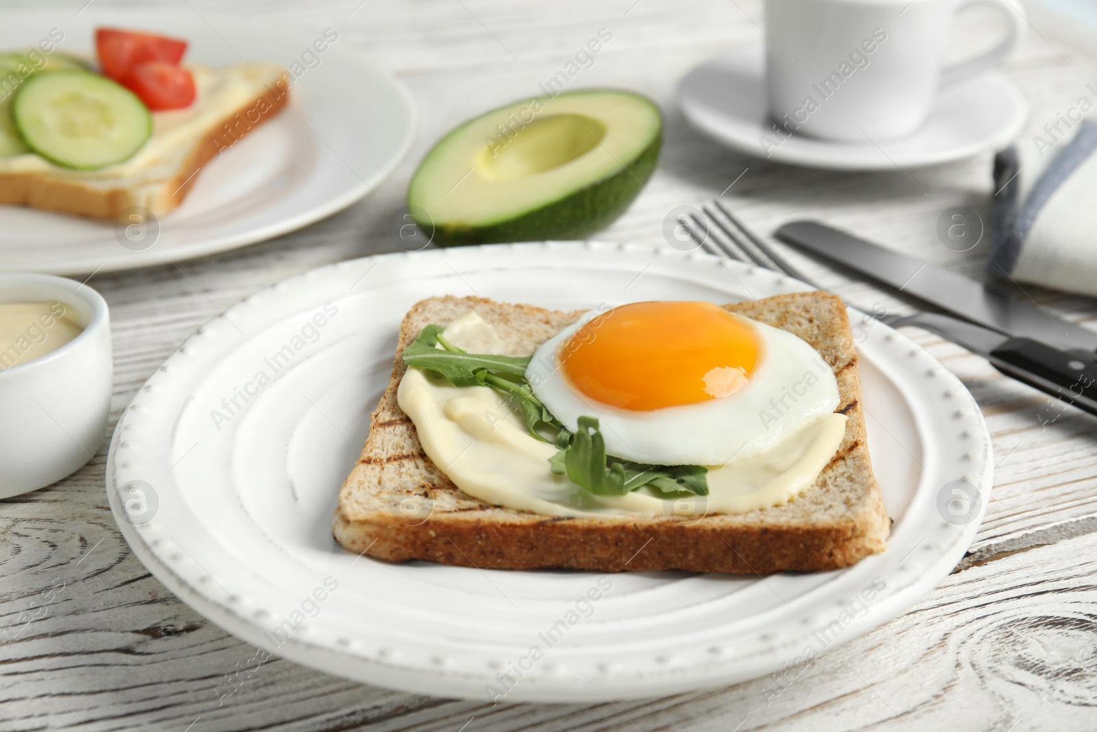 Photo of Slice of bread with fried egg, spread and arugula on white wooden table