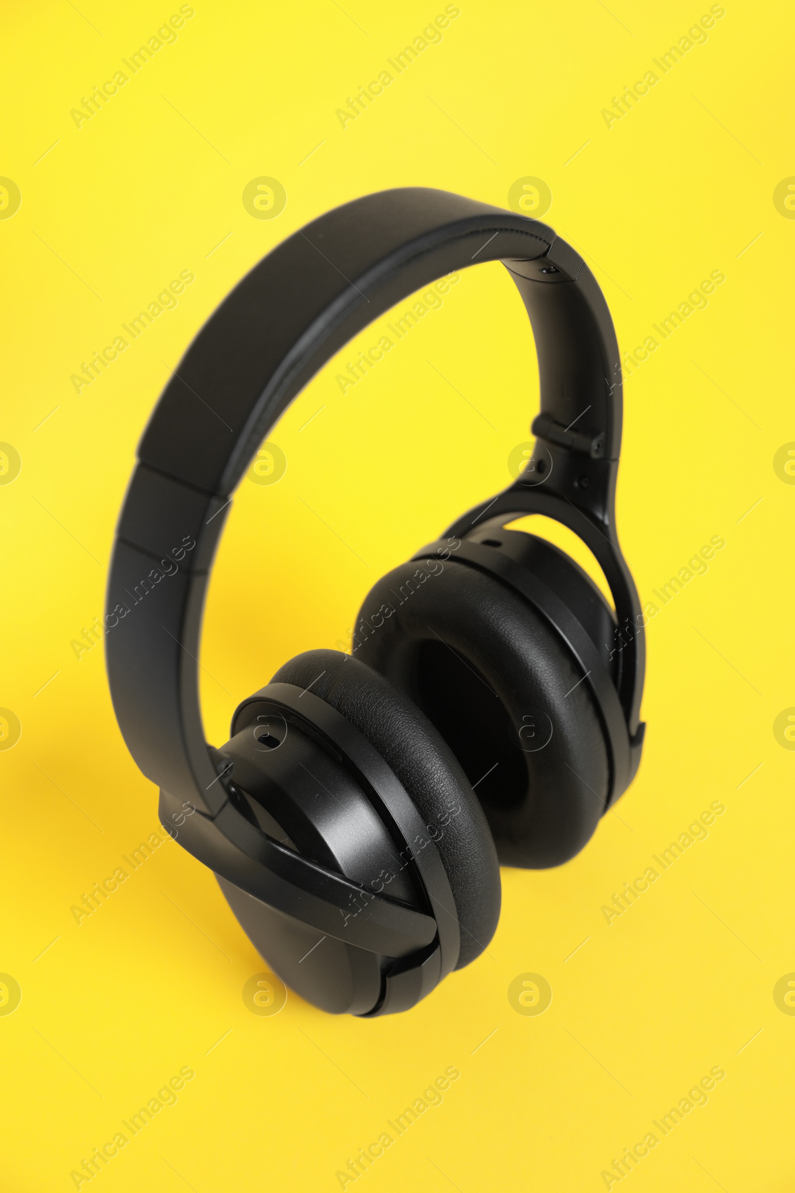 Photo of Modern black wireless headphones on yellow background