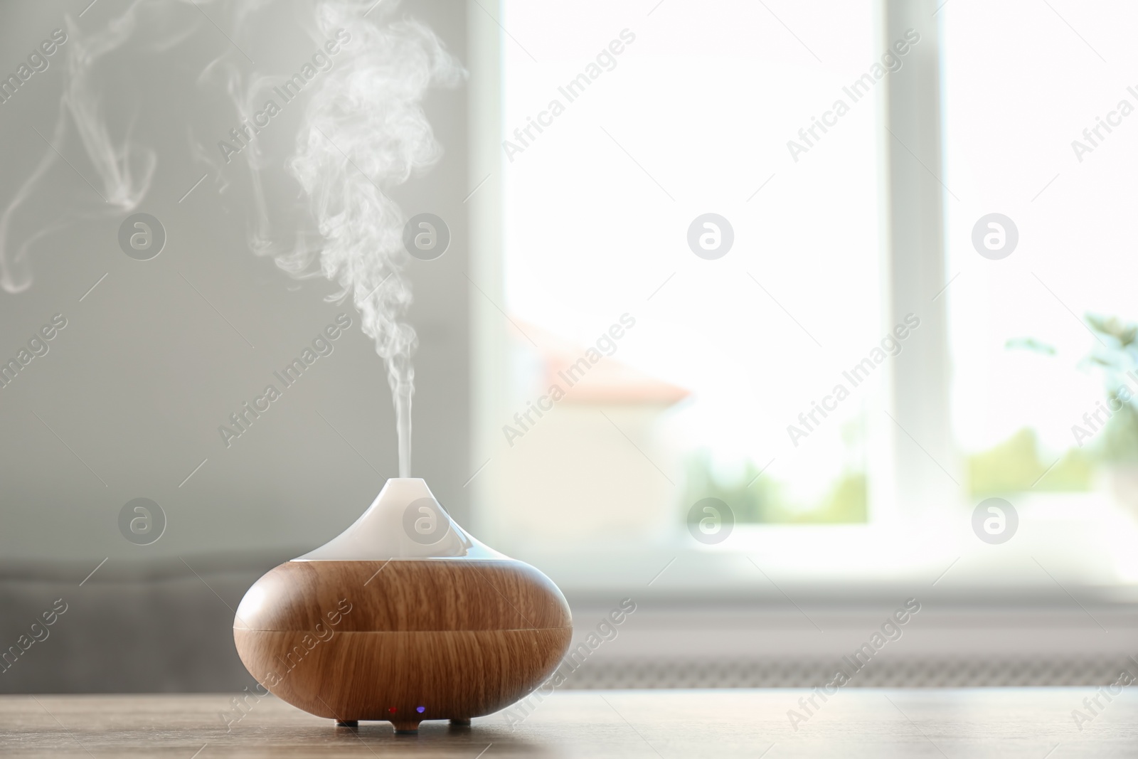 Photo of Modern aroma lamp on table against blurred background with space for text