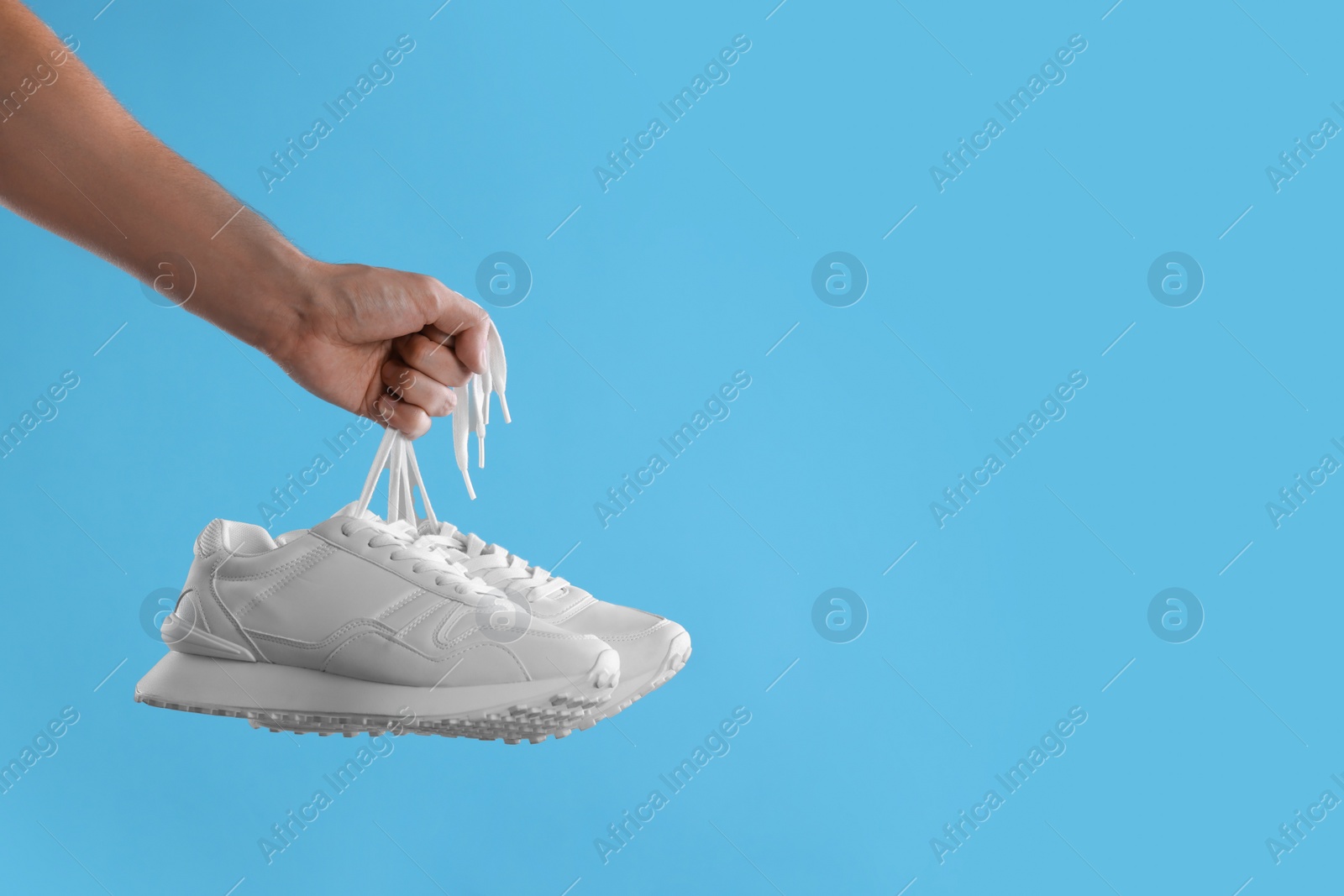 Photo of Man holding stylish sneakers on light blue background, closeup. Space for text