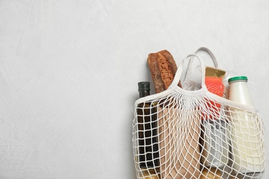 Mesh bag with different products on light grey background, space for text