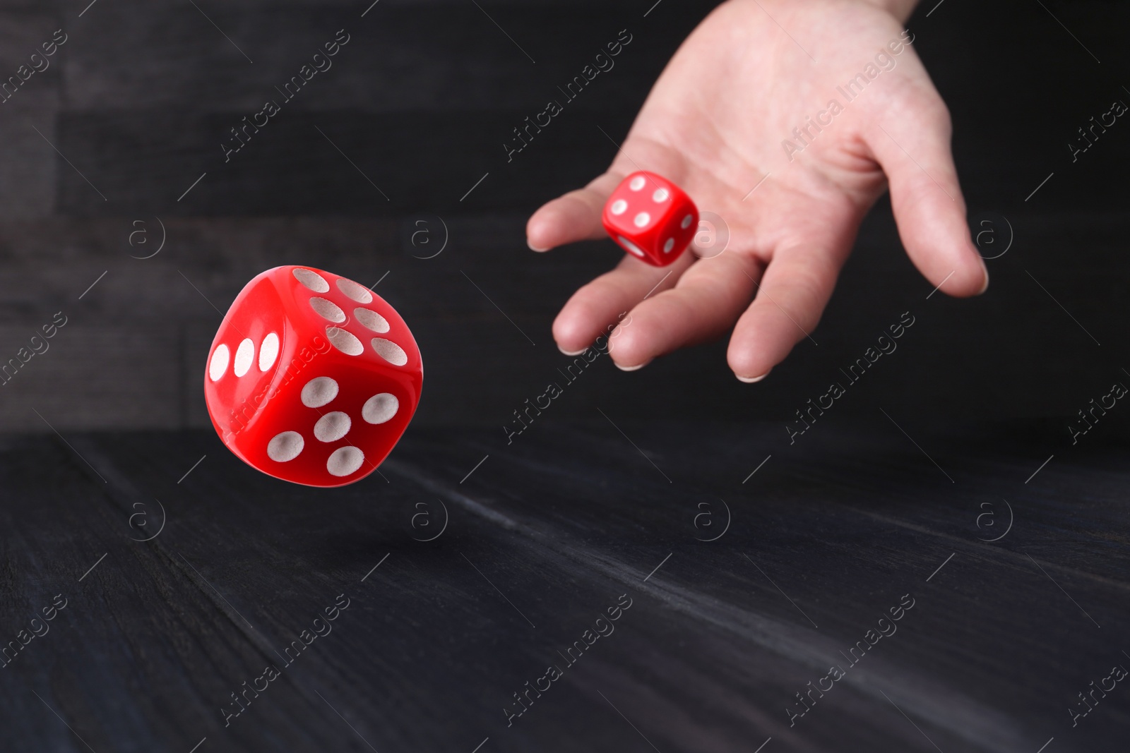 Image of Woman throwing red dice on black wooden table, closeup