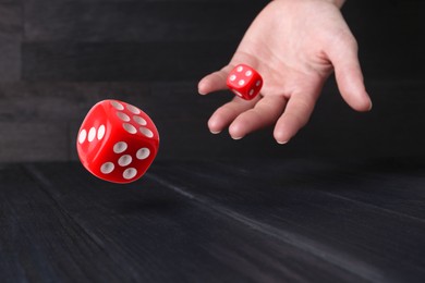 Image of Woman throwing red dice on black wooden table, closeup