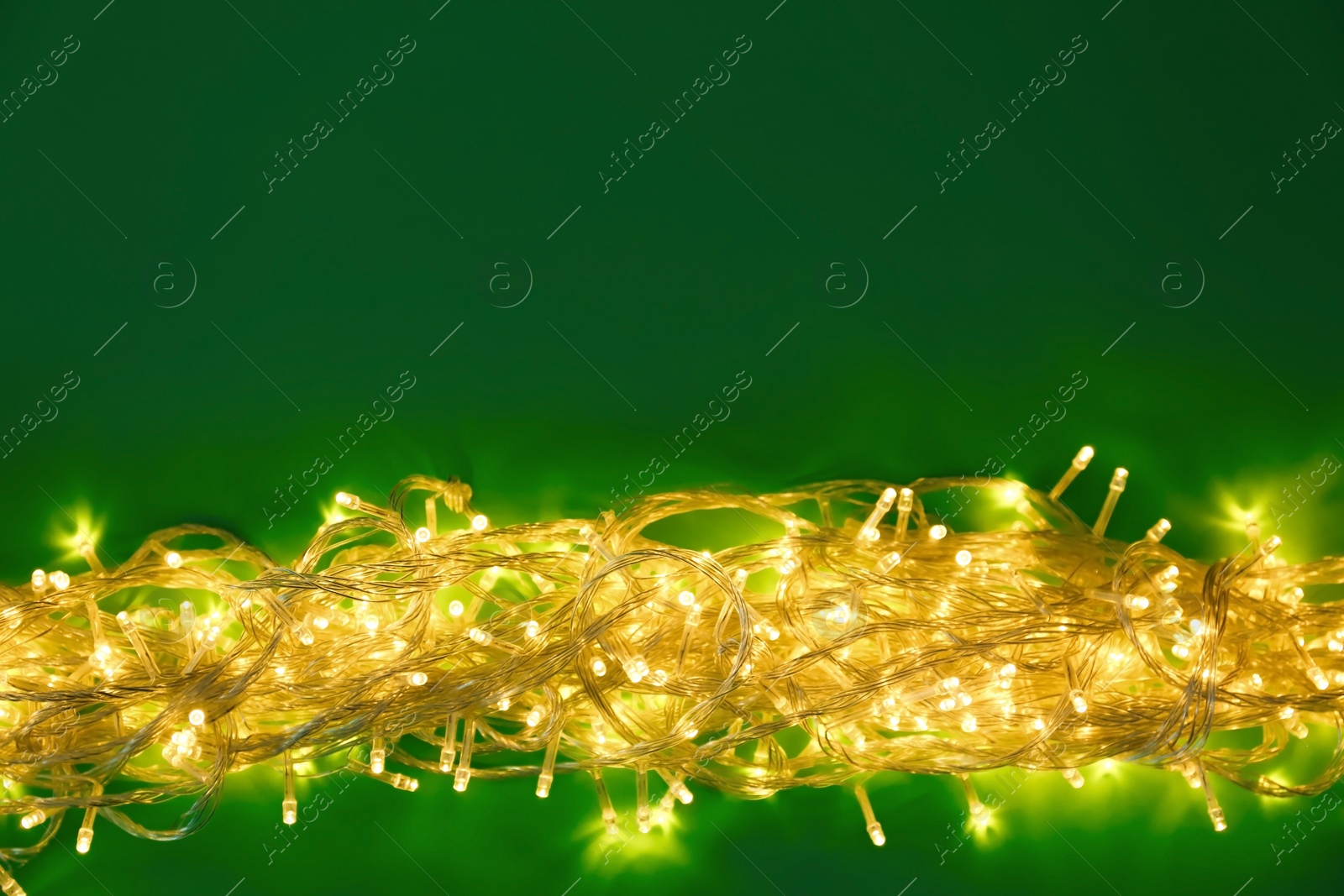 Photo of Glowing Christmas lights on green background, top view. Space for text