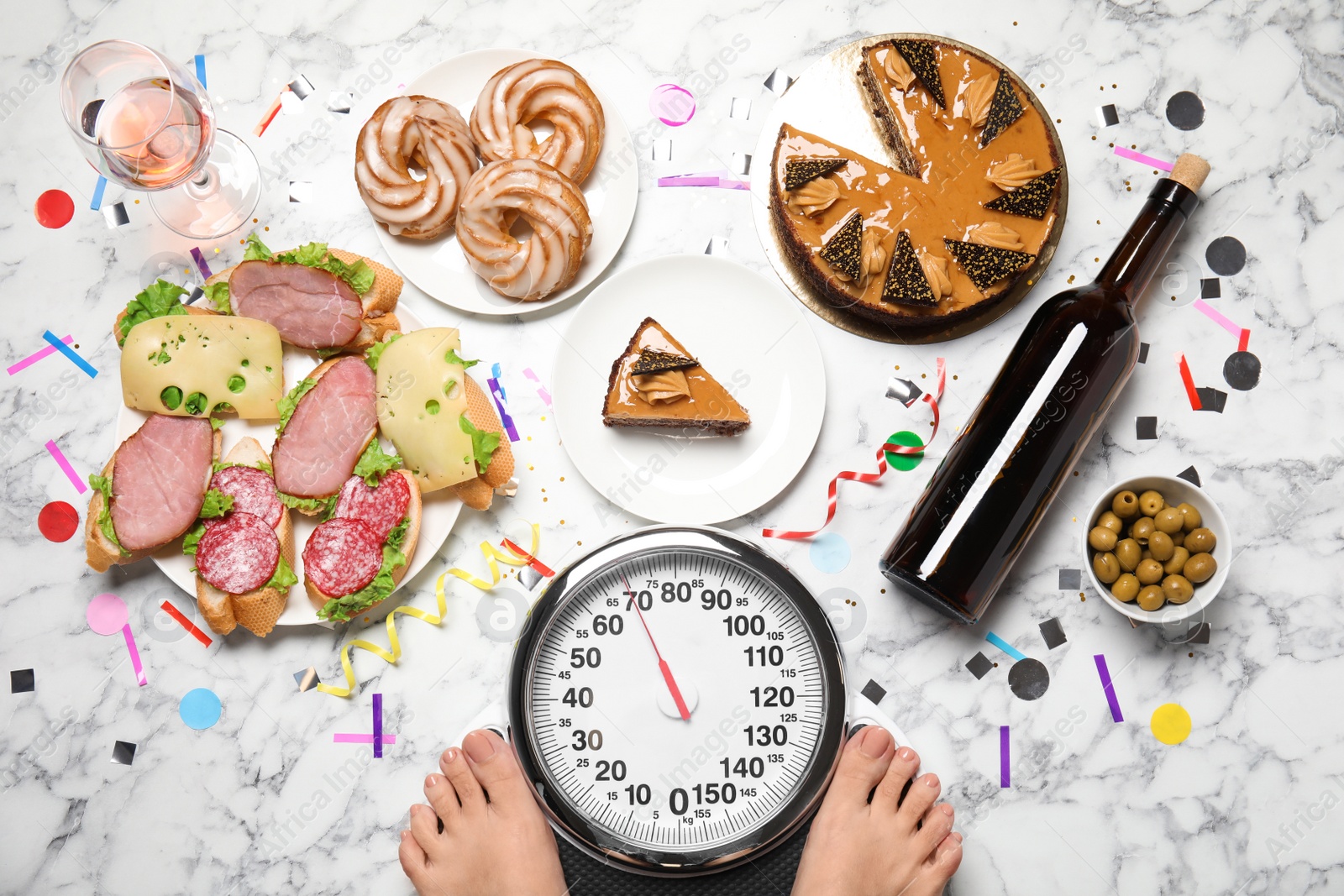 Photo of Woman using scale surrounded by food and alcohol after party on floor, top view. Overweight problem