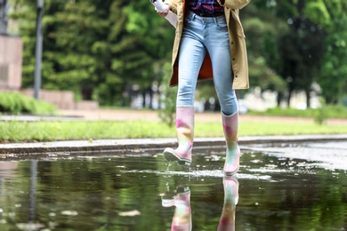 Woman with rubber boots running in puddle, closeup. Rainy weather