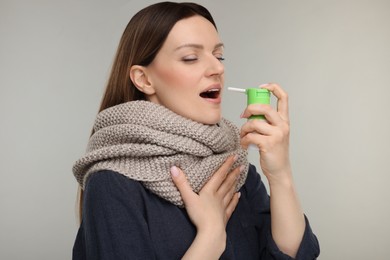 Woman with scarf using throat spray on grey background