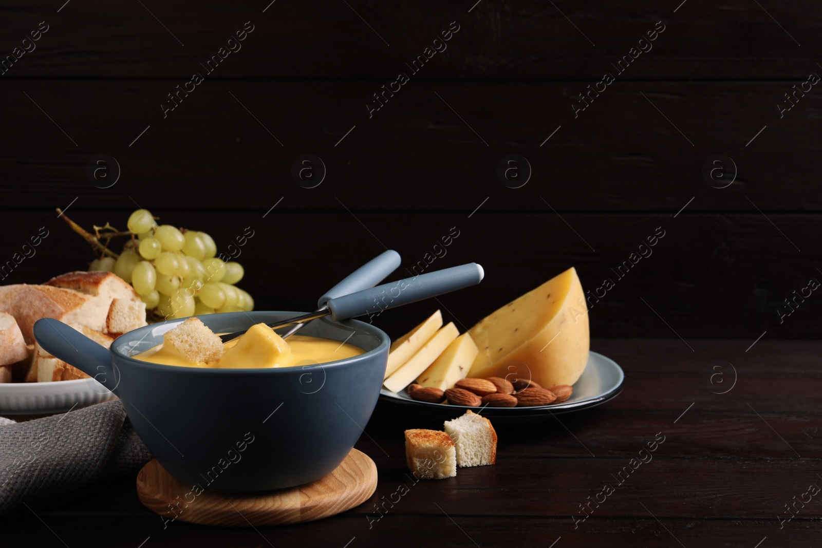 Photo of Pot of tasty cheese fondue and snacks on wooden table. Space for text