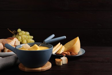 Photo of Pot of tasty cheese fondue and snacks on wooden table. Space for text