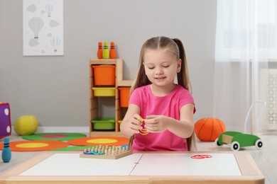 Photo of Motor skills development. Happy girl playing with geoboard and rubber bands at white table in kindergarten