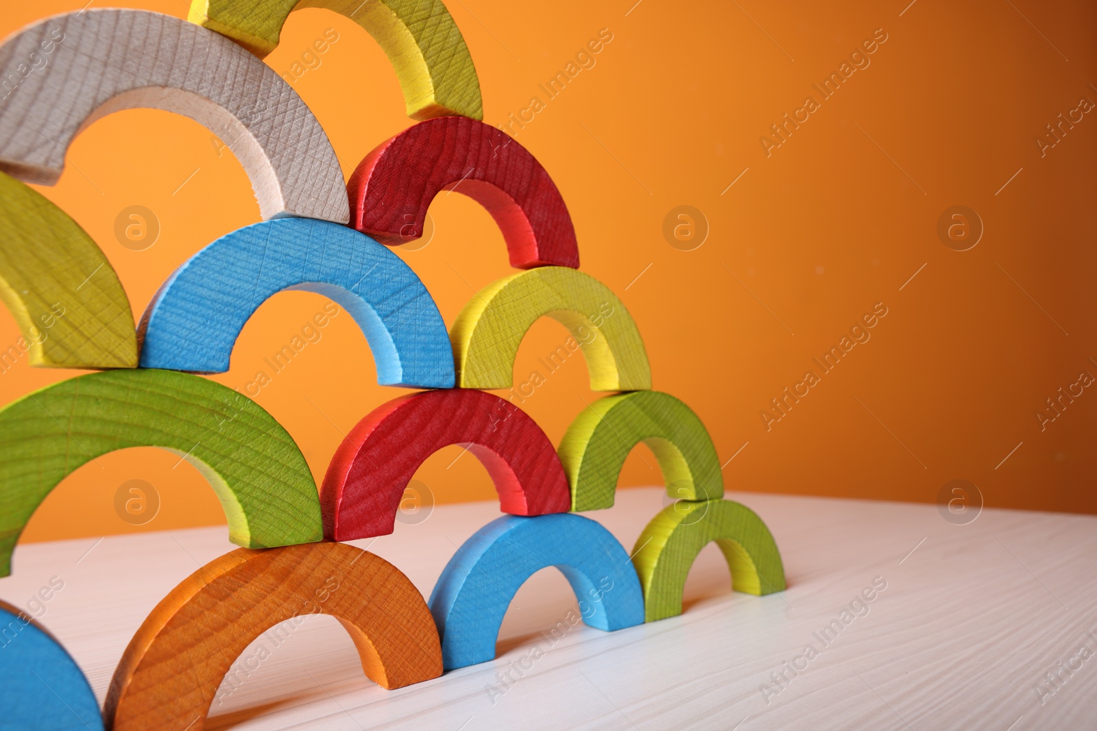 Photo of Colorful wooden pieces of educational toy on light table against orange wall, closeup and space for text. Motor skills development