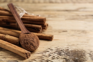 Photo of Aromatic cinnamon powder and sticks on wooden table, closeup. Space for text
