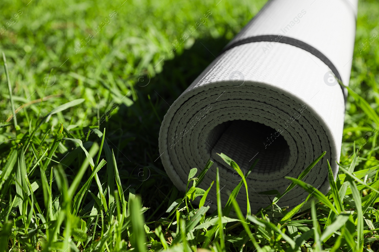 Photo of Rolled karemat or fitness mat on green grass outdoors, closeup. Space for text